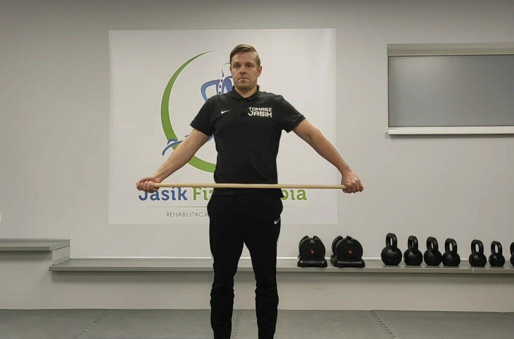 Mężczyzna wykonuje ćwiczenie z kijem w salonie rehabilitacji.